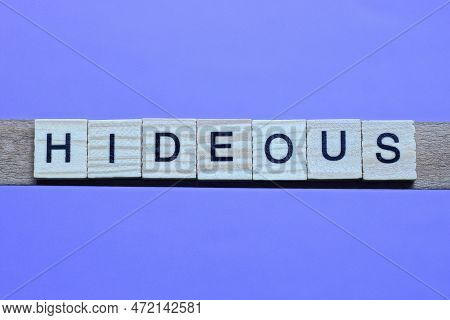 Word Hideous Made From Wooden Gray Letters Lies On A Lilac Background
