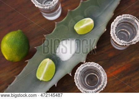 Mexican Tequila Shots, Salt, Lime And Green Leaf On Wooden Table, Flat Lay. Drink Made Of Agava