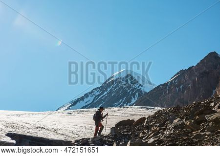 Scenic Alpine Landscape With Silhouette Of Hiker With Trekking Poles Against Large Glacier Tongue An