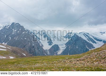 Scenic Alpine View From Sunlit Green Grassy Hill To High Snowy Mountain Range With Sharp Tops And Gl
