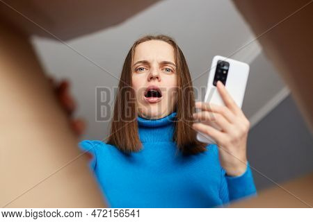Astonished Caucasian Young Adult Woman Wearing Blue Turtleneck Opening Carton Box, Looking Inside Pa