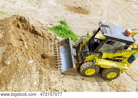 A Mini Tractor-loader Moves And Loads Earth On A Construction Site.