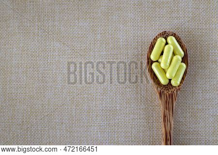Capsules Yellow Quercetin In A Wooden Spoon On A Beige Background. Top View, Copy Space.