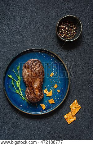 Grilled Spiced Marbled Beef Steak With Microgreens And Crispbread On Black Background. The Shape Of 