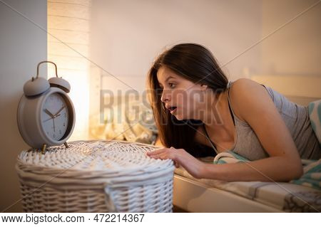 A Girl With Long Hair In Shock Checks The Time On Her Alarm Clock.