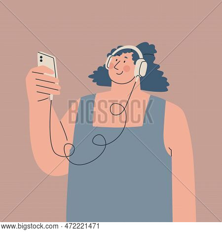 Cute Young Woman Wearing Over-ear Headphones On Her Head And Holding A Smartphone In Her Hand. Perso