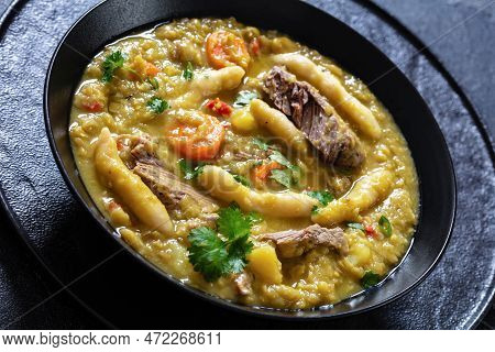 Close-up Of Gungo Peas, Pigeon Peas Soup With Dumplings , Vegetables And Beef In Black Bowl On Concr