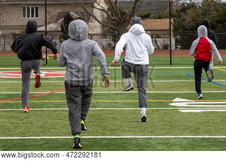 Rear View Of Rhigh School Track Unners Performing Speed Sports Drills On A Turf Field In The Cold.