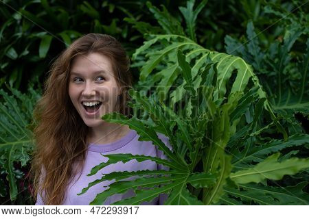 Portrait Of Young Woman Standing On An Ivy, Fern Wall Or In Greenery, Breathing, Smiling And Looking