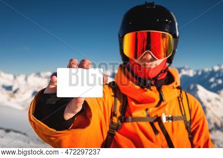Snowboarder Holds An Empty Lift Pass With A Mountain In The Background. A Young Man Is Holding An Em
