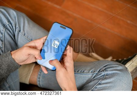 Top View Of A Man In Jeans Sits On The Floor Using Linkedin Mobile Application On His Phone.