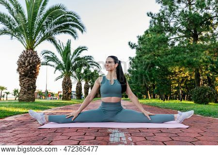 Sportive And Smiley Athletic Young Female Fitness Coach In Sportswear Sits In The Leg-split On The Y