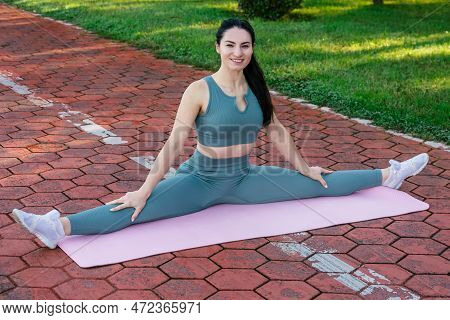 Sportive And Smiley Athletic Young Female Fitness Coach In Sportswear Sits In The Leg-split On The Y
