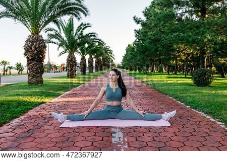 Sportive And Smiley Athletic Young Female Fitness Coach In Sportswear Sits In The Leg-split On The Y