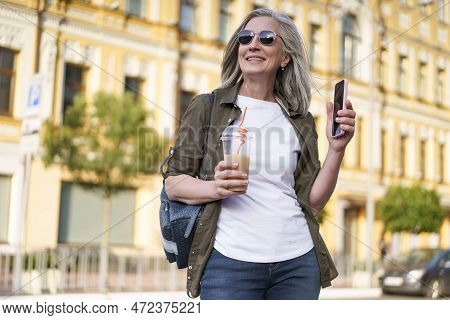 Biohacking Concept. A Mature European Woman With Gray Hair Wearing Sunglasses Walks Around The City 