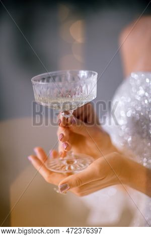 The Hands Of A Woman Hold A Glass Of Champagne On A Background Of Golden Beke. The Concept Of The Ho