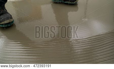 Construction Worker Applying Grey Epoxy Resin In An Industrial Hall. Closeup Shot Of A Worker Applyi
