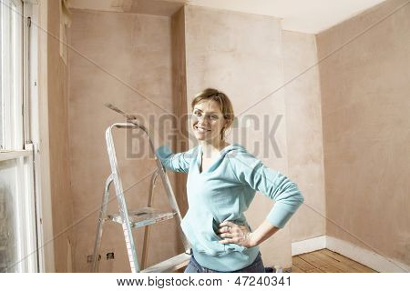 Portrait of happy woman holding scraping tool in unrenovated room