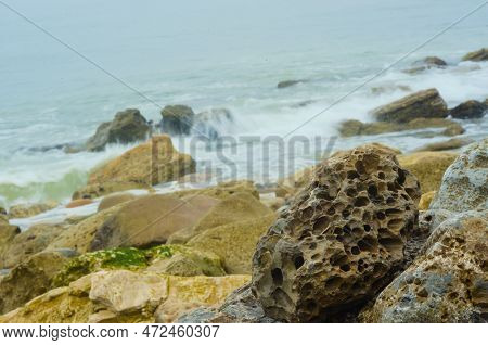 Hole-riddled Stones Lay On A Rocky, Rugged Shoreline