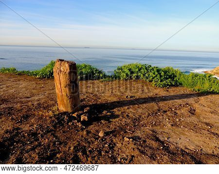 A Weathered Post Casts A Long Shadow Along A Seaside Cliff, With The Sky Meeting The Ocean On The Di