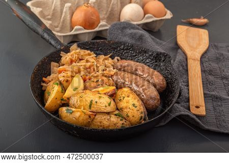 Baked Potato Wedges, Grilled Sausages And Stewed Cabbage Cooked In An Old Cast Iron Skillet. Close-u