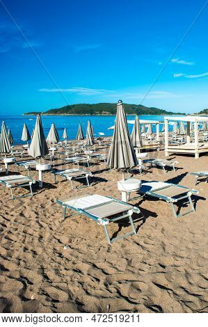 Sun Loungers And Umbrellas On Public Beach At Summer Sunny Mornin. Skojl Island Background. Calm Sea