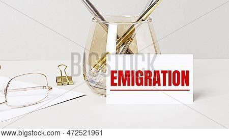 Work Desk With Gold Glasses, Pen, White Card With The Text Emigration. Business Concept. Home Office