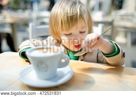 Cute Toddler Boy Having Hot Chocolate In Outdoor Cafe. Small Child Drinking Hot Beverage On Sunny Te