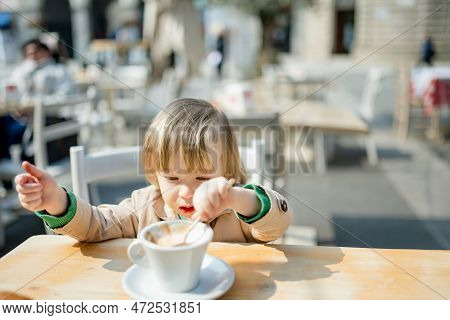 Cute Toddler Boy Having Hot Chocolate In Outdoor Cafe. Small Child Drinking Hot Beverage On Sunny Te