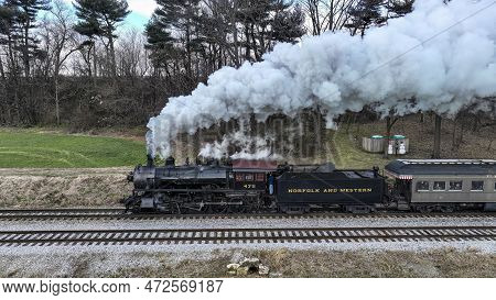 A Side Drone View Of A Steam Locomotive Approaching Traveling Thru Fields And Meadows, Blowing White