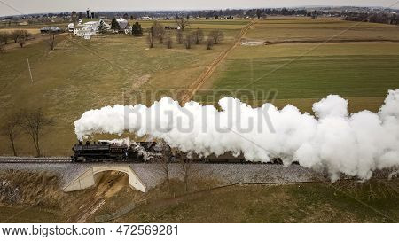 A Side Aerial View Of A Steam Passenger Train Approaching, Traveling Thru Open Farmlands, Blowing Lo