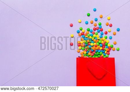 Shopping Paper Gift Bag In Corner Full Of Assorted Traditional Candies Falling Out On Colored Backgr
