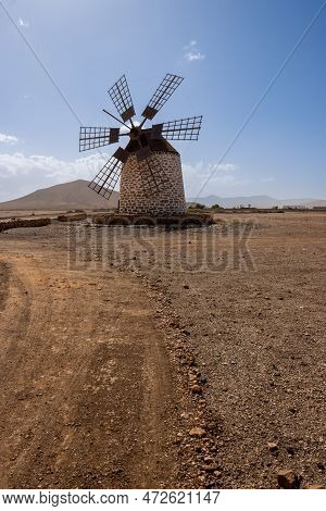 Old Traditional Windmill, Located In A Stone Desert. Blue Sky With Some White Clouds In The Winter. 