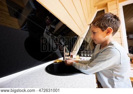 Boy Washes Hands In The Sink At Kitchen  In Cozy Wooden Tiny Cabin House. Life In Countryside.