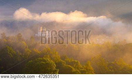 Castle Rozmberk Shrouded In Morning Mist Illuminated By The Rising Sun. Rozmberk Nad Vltavou, Czech 
