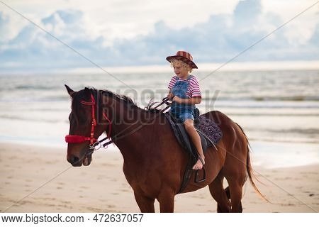 Kids Riding Horse On Beach. Children Ride Horses. Cute Blond Kid In Cowboy Hat With Usa Flag On Summ