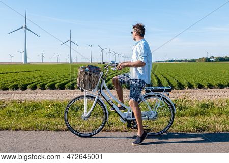 Young Man Electric Green Bike Bicycle By Windmill Farm , Windmills Isolated On A Beautiful Summer