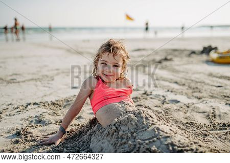 Little Girl Buring Herself In Sand, Enoying Summer Vacation At Sea.