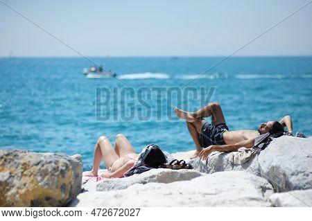 San Terenzo, Italy - May 2011: Man And Woman Wearing Swimming Suits Sunbathing On A Rocky Beach Of S