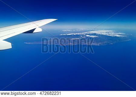 Aerial View Through Porthole Of Plane To Island In The Mediterranean Sea. Scenic View Through Aircra