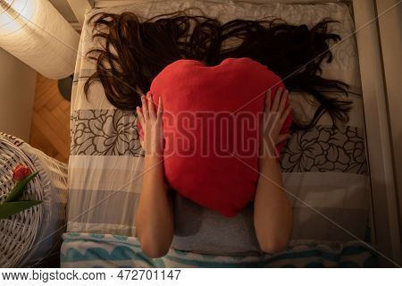 The Girl Covers Her Face With A Red Heart-shaped Pillow.