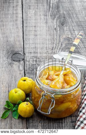 Homemade  Quince Jam In Glass Jars And Fresh Quince With Leaves On Wooden Table