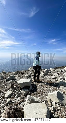Asian Man Standing On Top Of A Nearby Mountain Looking At Mount Sindoro. West Java, Indonesia, March