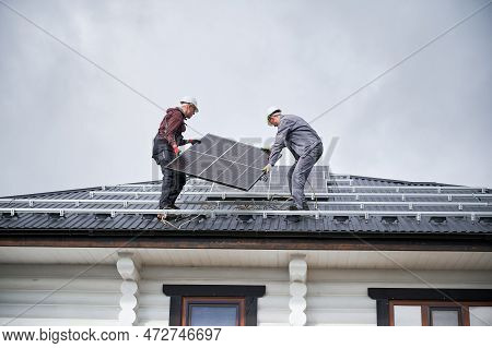 Mounters Building Solar Panel System On Roof Of House. Men Workers In Helmets Carrying Photovoltaic 