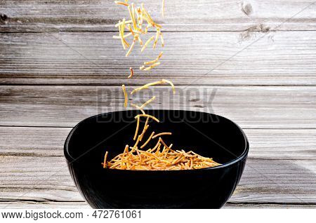 Close-up Of Cooked Polyphosphate Noodles Falling Into A Ceramic Bowl On A Wooden Table