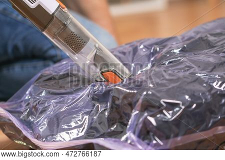A Man Removes Air From A Vacuum Bag Using A Manual Vacuum Cleaner. Winter Jackets In A Vacuum Bag Fo