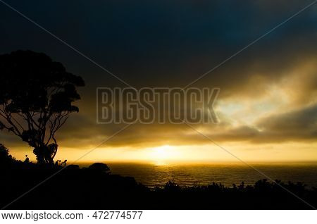A Dramatic Coastal Sunset On A Cloudy Day Turns The Sky A Brilliant Gold With Blue And Silver Accent