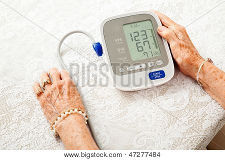 Gros plan des mains de la femme senior vérifier sa pression artérielle sur un compteur à domicile.  Les résultats sont faibles.