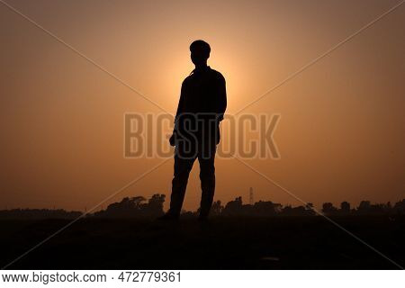 Man Silhouette, Standing On A Rural Field And Looking Straight. Silhouette Of A Man With A Sunset Vi
