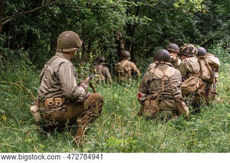 Historical Reconstruction. World War Ii Infantry Division Soldiers Patrol A Site In The Tall Grass. 